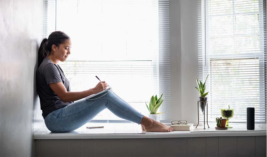 woman sitting in a windowsill writing in a notebook