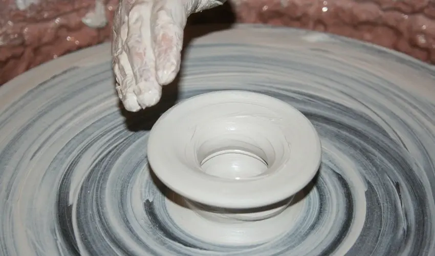 Hand shaping a clay pot on a spinning pottery wheel, with wet clay forming concentric patterns.