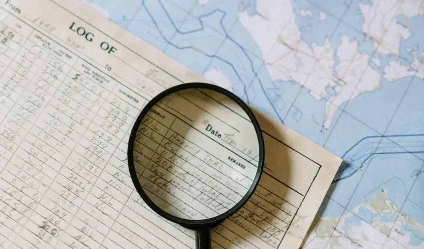 Close-up of a magnifying glass placed over a handwritten log sheet, with a nautical map in the background.