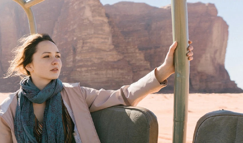 Girl with a scarf and jacket in the backseat of an open vehicle looking off into the desert
