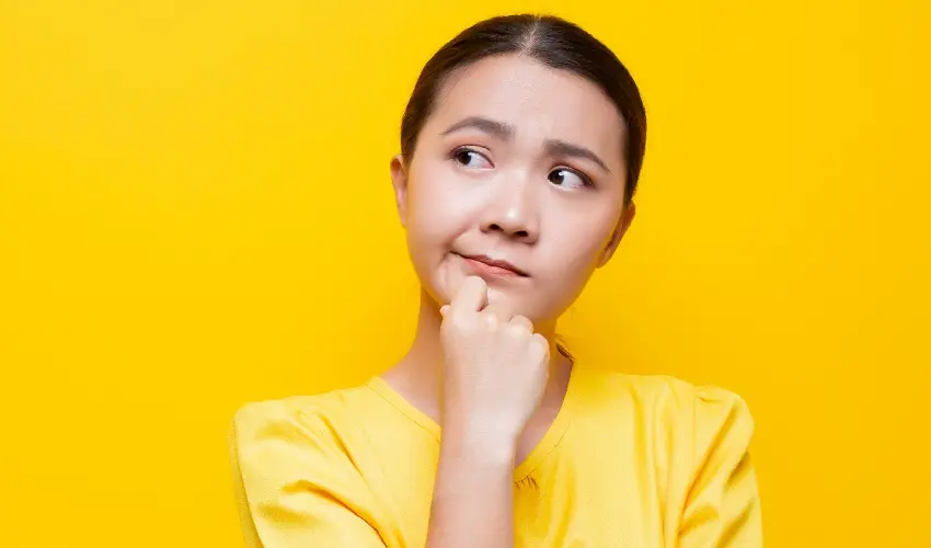 Pensive woman in a yellow shirt with a yellow background.