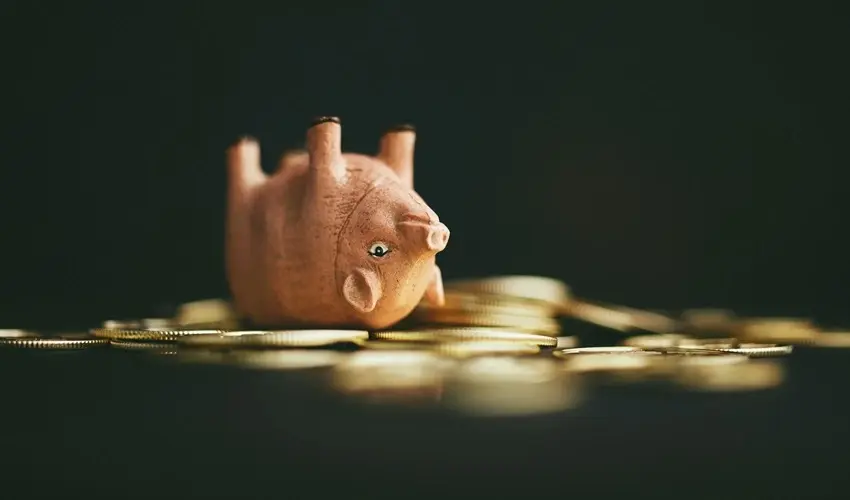 Small piggy bank flipped upside down on a pile of gold coins, set against a dark background.