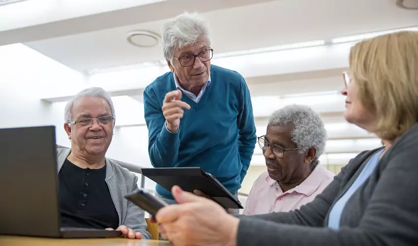 older people standing around a table looking at tablets
