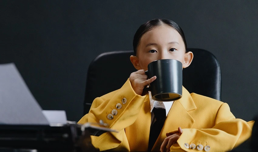 Little girl in yellow suit at a desk drinking from a black mug