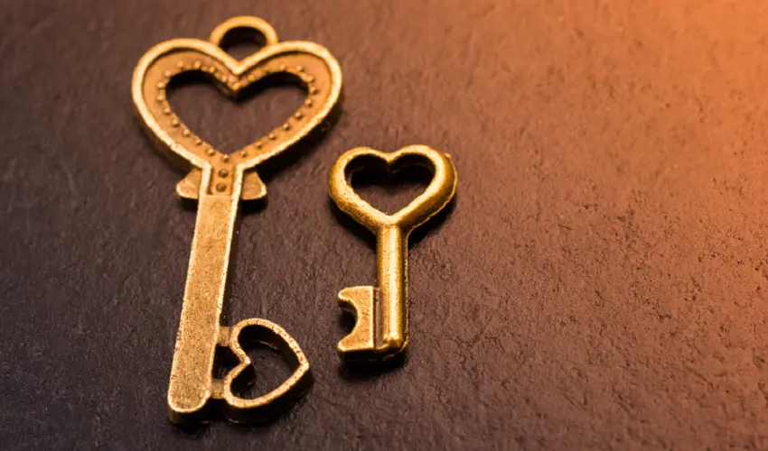 Two golden heart keys facing each other on a brown gradient background