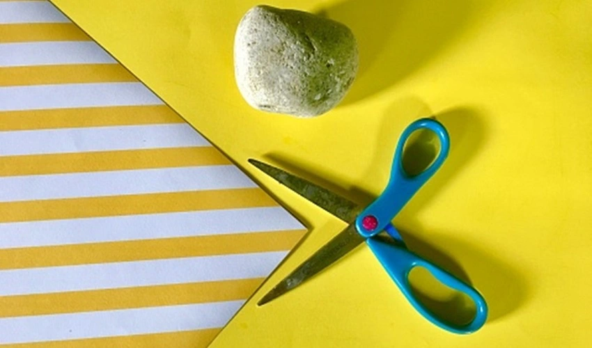 rock, blue scissors, and a yellow and white striped piece of paper on a bright yellow background