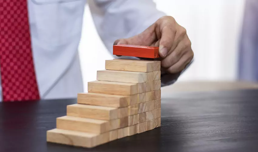 hand stacking red block on top of a staircase of wooden blocks