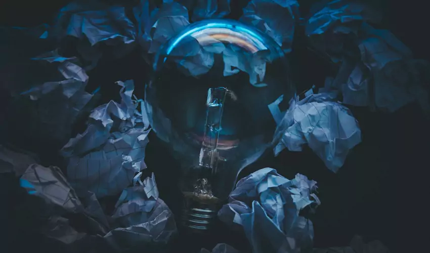 Lightbulb surrounded by crumpled paper in blue light
