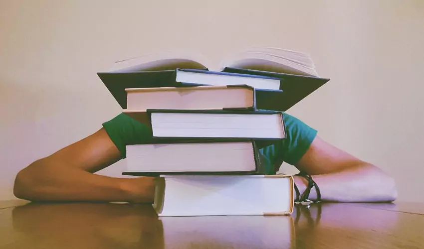 Books stacked in front of student with crossed arms