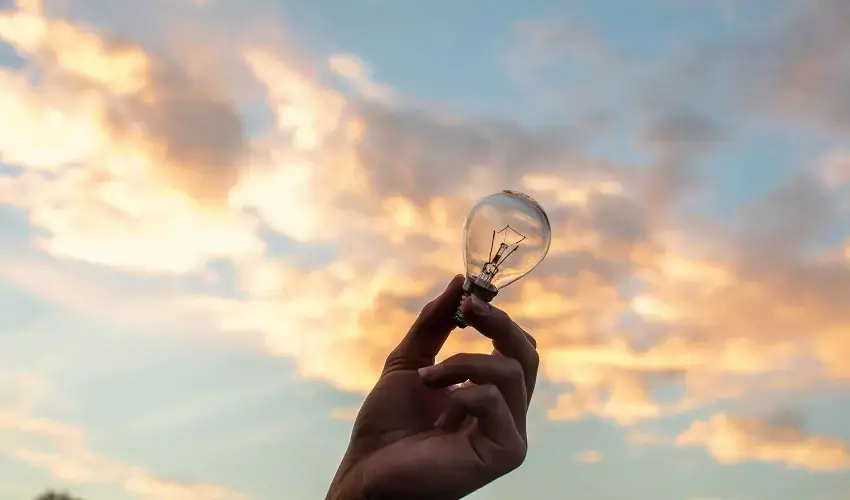 Hand holding lightbulb in sunset