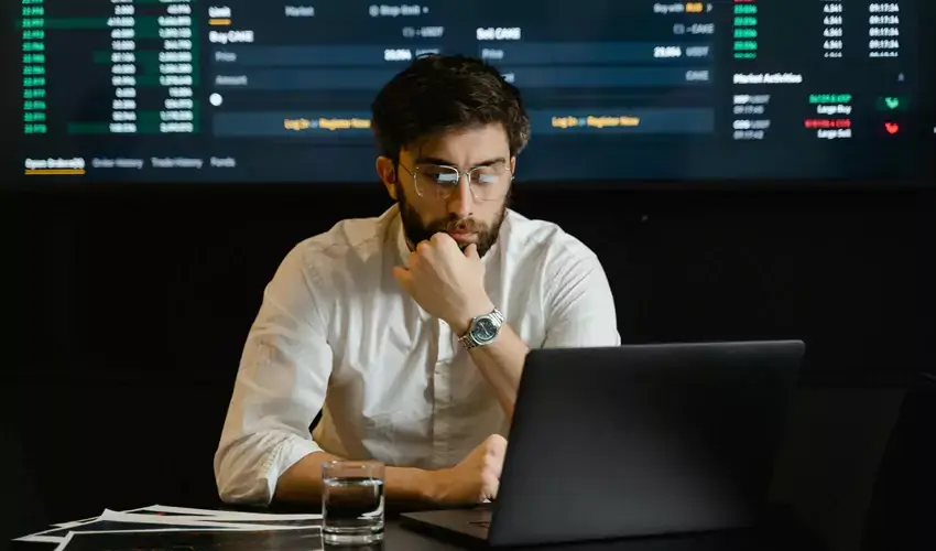 Man looking at laptop with investment info behind him