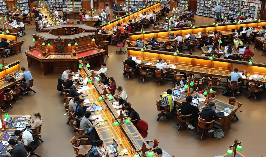 dozens of people sitting at desks in a large library