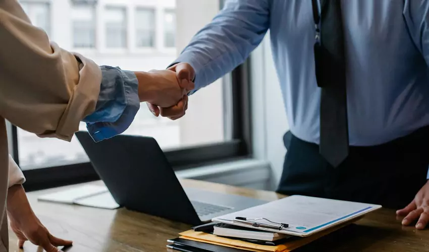 Two people shaking hands over desk