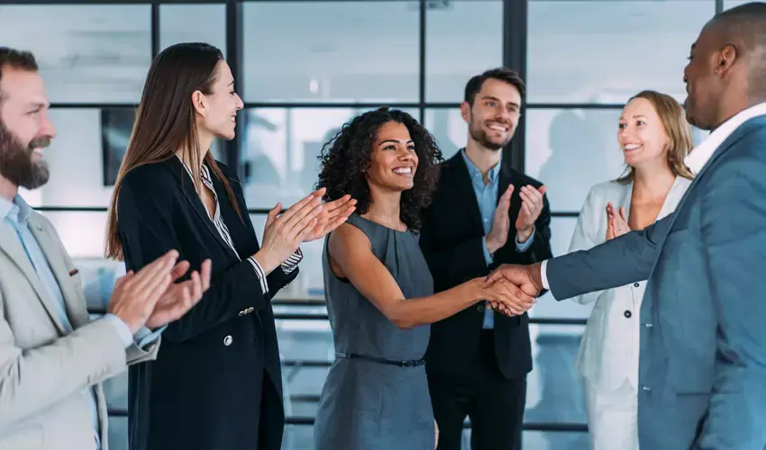 two business people shaking hands while others clap around them