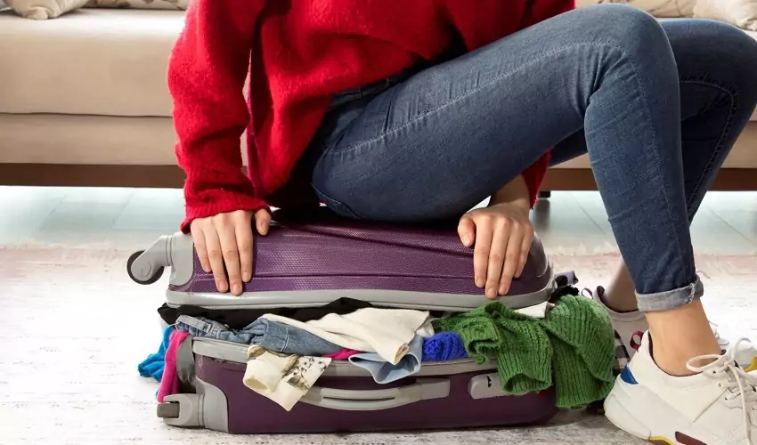 Woman sitting on overflowing suitcase